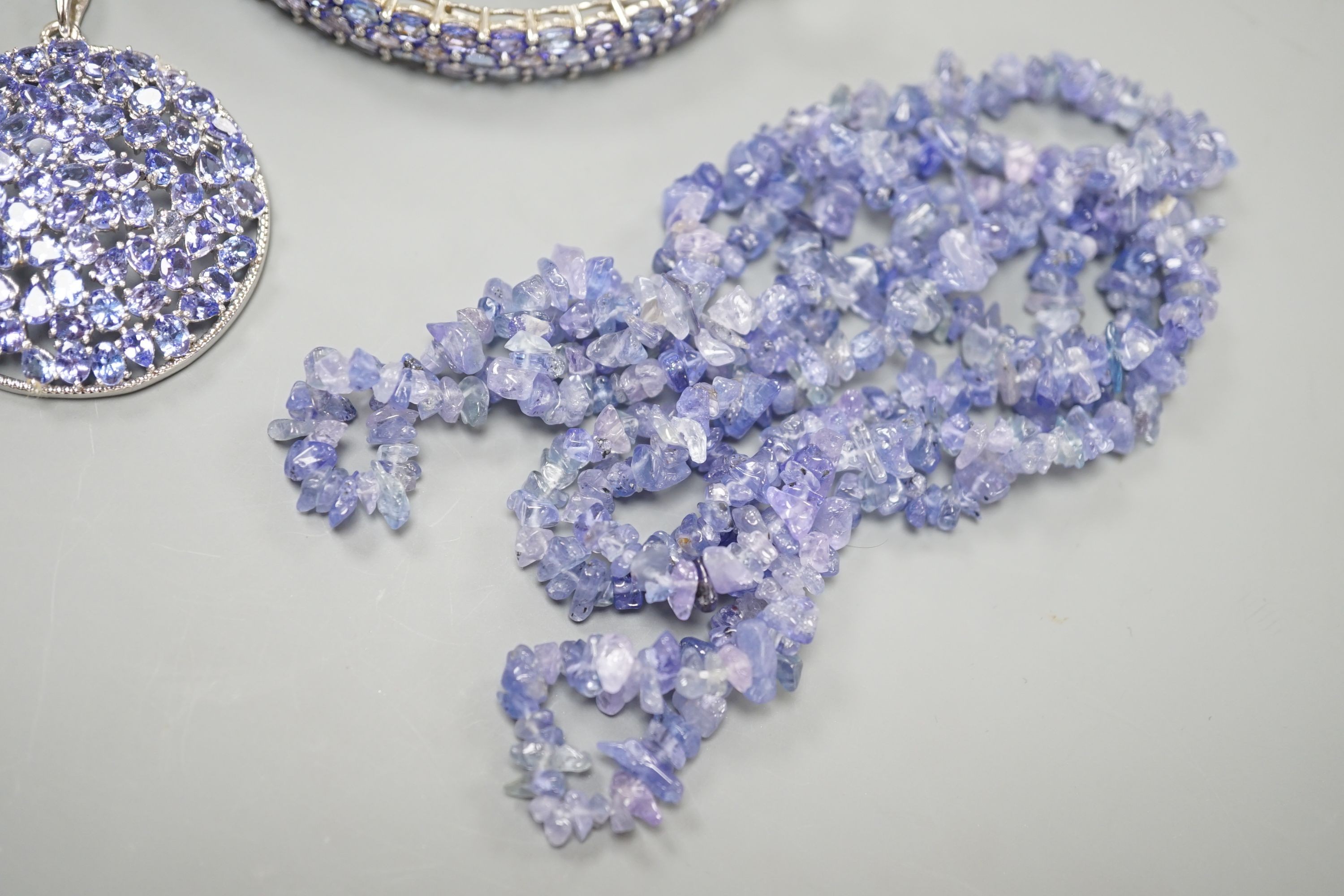 A modern 925 and tanzanite set hinged bangle, a similar pair of earrings and pendant and a rough cut tanzanite set necklace.